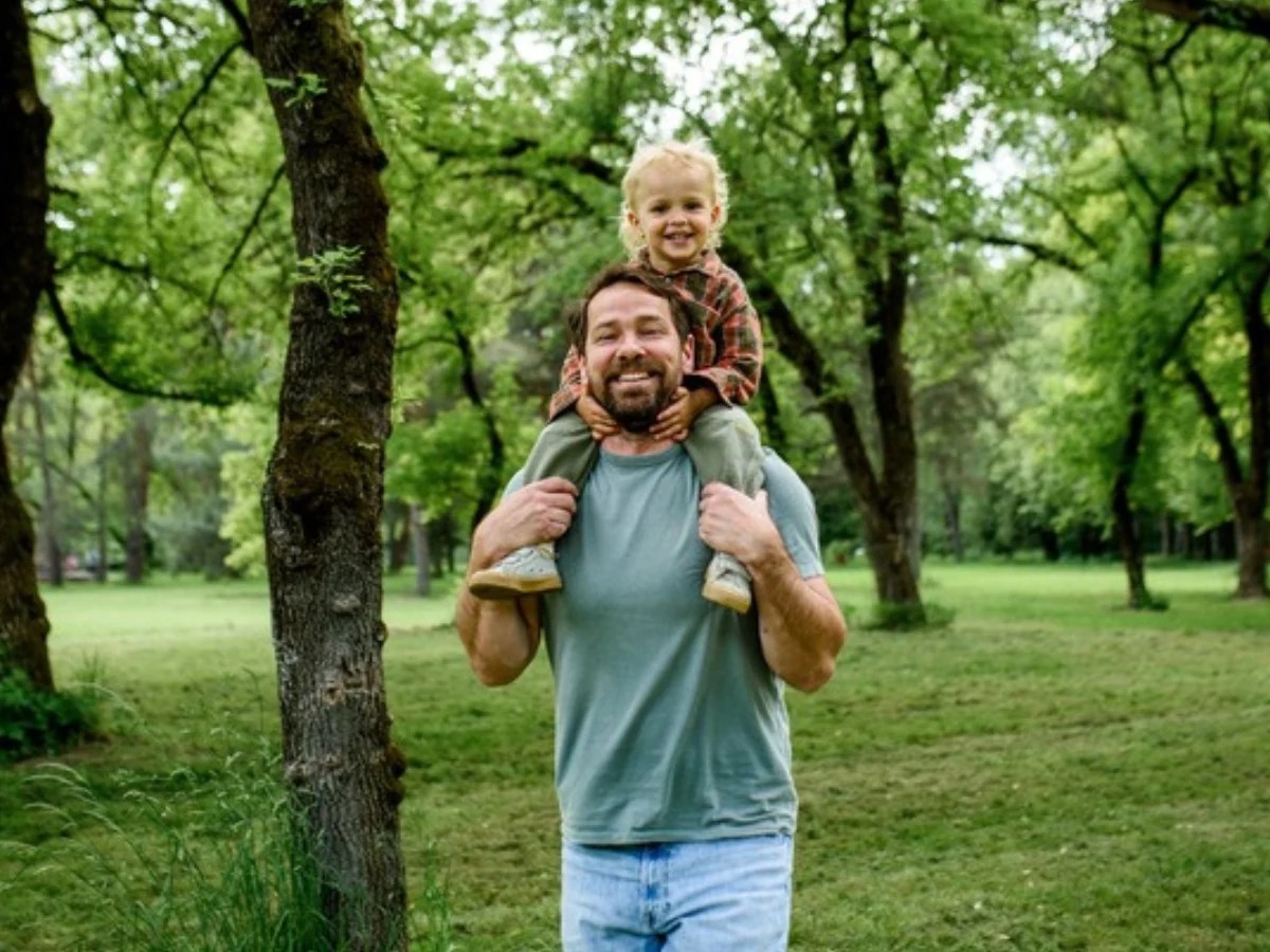 A father carrying a child on his shoulders in a park